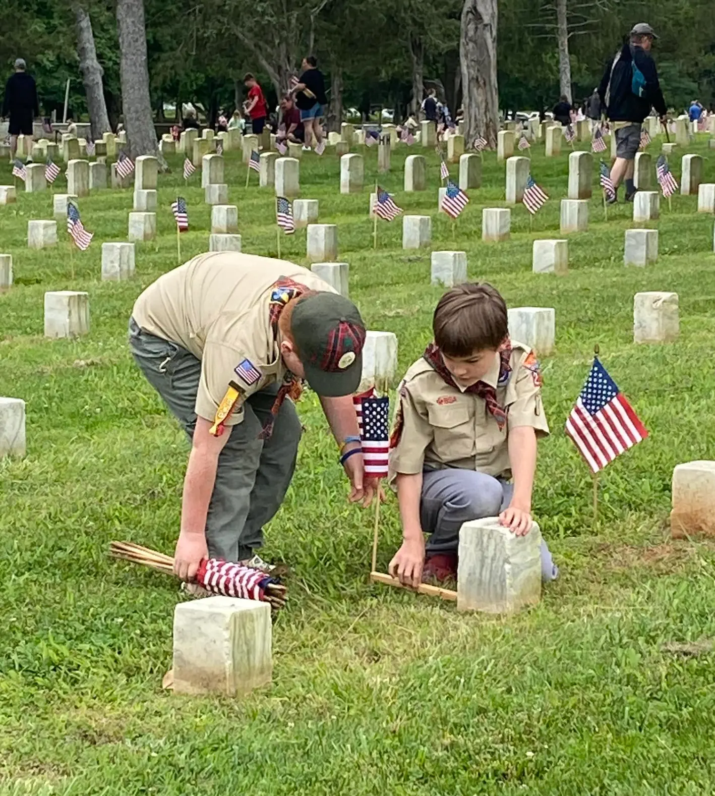 A Scout and leader placing flags at a veterans cemetery